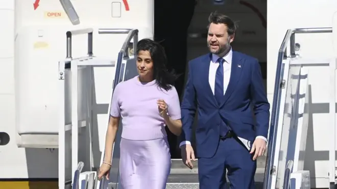 A man and woman in lilac walk down steps from a plane