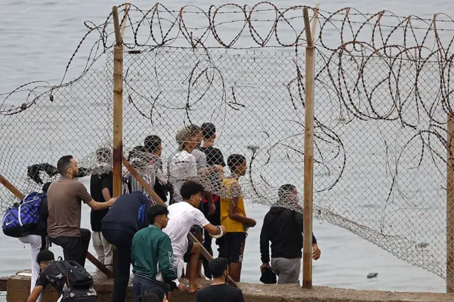 Migrantes cruzan una valla en Ceuta