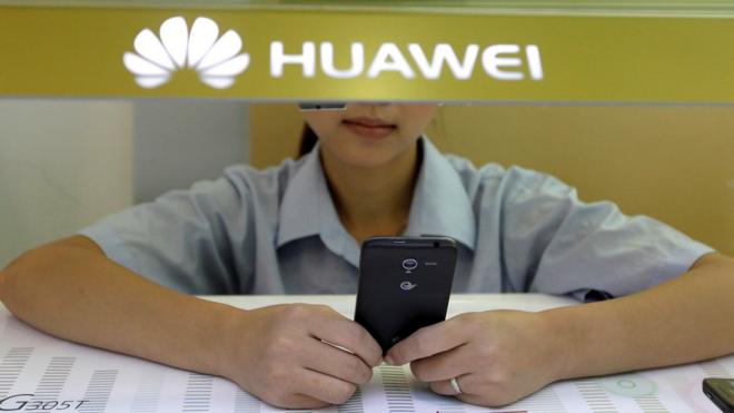 A sales assistant looks at her mobile phone as she waits for customers behind a counter at a Huawei booth in Wuhan, China