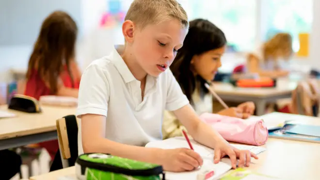 Niño en un salón de clase escribiendo con lápiz