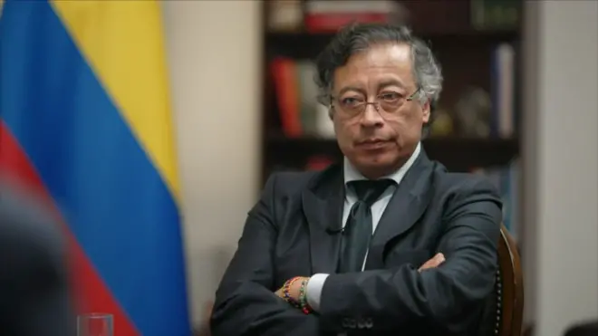 Colombia's president sits with his arms crossed and a stern expression. He wears a dark suit and tie. 