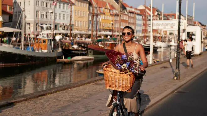 Joven feliz con gafas de sol disfrutando mientras pasea en bicicleta por el muelle de Nyhavn en la ciudad.