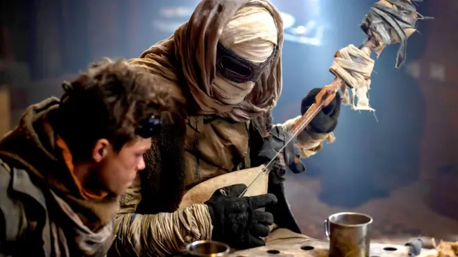 дечак поред мушкарца умотаног у завоје и огрнутог крпама који свира на гуслама -  сцена из филма Воља синовљева