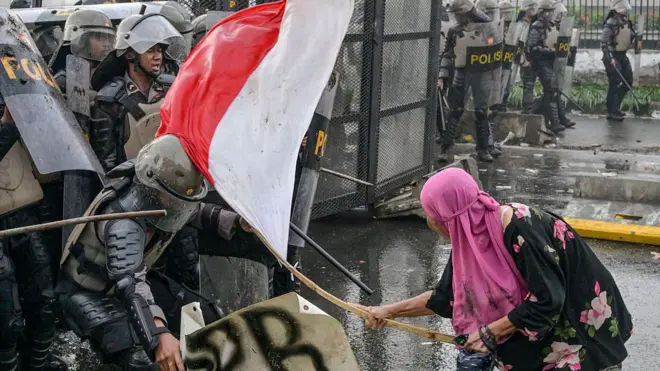 Seorang demonstran perempuan memukul petugas polisi dengan tongkat bambu yang diikatkan bendera Indonesia saat aksi demo 28 Agustus 2025.