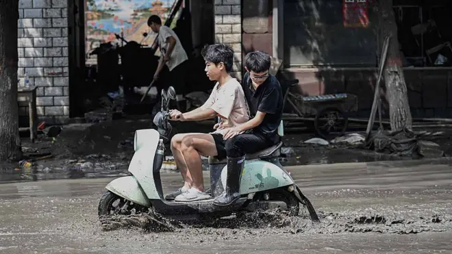 两名男性驾驶电动车行驶在淹水的街道