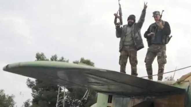  rebel fighter gestures the victory sign while standing on a military aircraft that belonged to forces loyal to Bashar al-Assad government, inside Hama's military airport, 7 December 2024