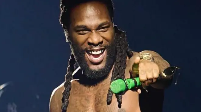 Umuririmvyi wo muri Nigeria Burna Boy ariko aririmba atagahuzu ko hejuru yambaye mu gihe afashe mikoro isa n'urwatsi rutoto.