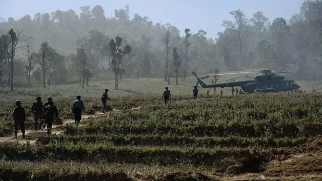 စစ်ရဟတ်ယာဥ်တစ်စင်းဆီ သွားနေတဲ့ မြန်မာစစ်တပ်တပ်ဖွဲ့ဝင်တွေ။ တောင်ပေါ်ဒေသမှာဖြစ်ပြီး လယ်ကွက်တစ်ခုကို ဖြတ်သွားနေတာဖြစ်ပါတယ်။