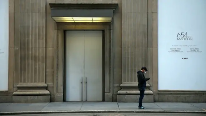 Seorang warga kota New York mengecek telepon selulernya di depan sebuah pertokoan yang tutup selama pandemi virus corona.