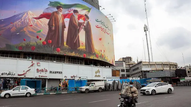 10 Mart 2026’da Tahran’ın merkezindeki Valiasr Meydanı’nda bir motosikletli, İran’da eski dini liderleri Ayetullah Hümeyni, Ayetullah Ali Hamaney ve yeni dini lider Mücteba Hamaney’in yer aldığı bir afişin önünden geçiyor.