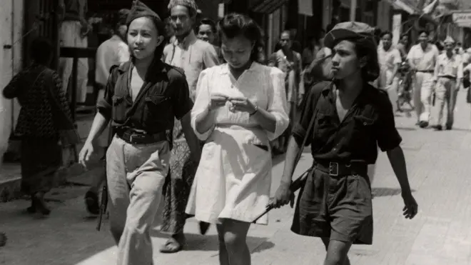 Tiga perempuan muda Indonesia di jalan. Dua di antaranya adalah relawan Republik Indonesia dari Sulawesi, anggota angkatan bersenjata muda KRIS, di Yogyakarta, Desember 1947. Foto karya Hugo Wilmar dari Arsip Nasional Belanda.