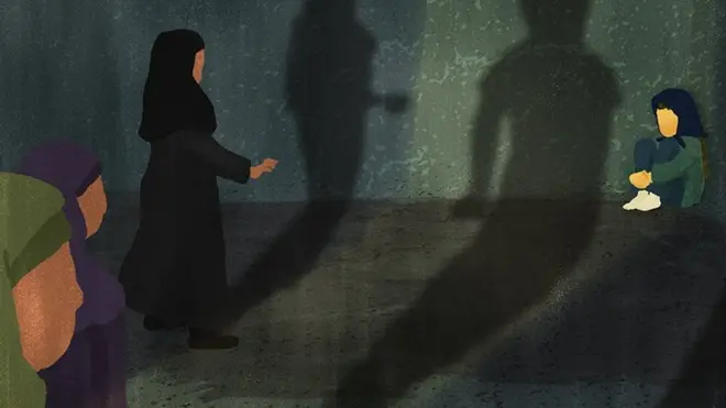 Three women approach a frightened girl, who is sitting in a ball in the corner of a dark room. Their shadows appear menacing.