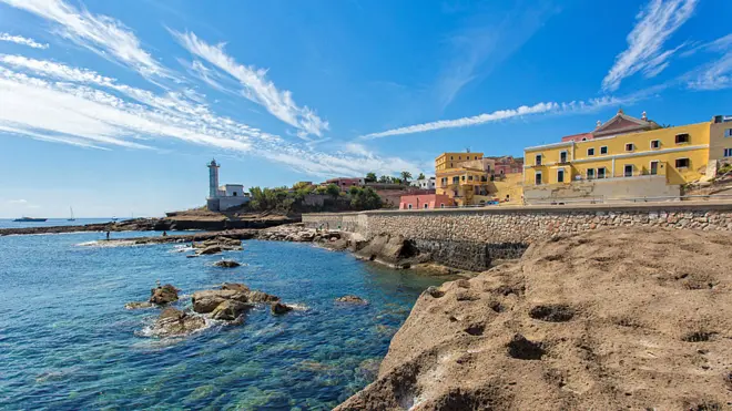 Vista do mar, de prédios e quebra-mar em Pandataria sob céu azul e ensolarado