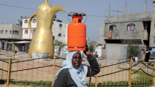 Une femme porte une bouteille de gaz sur la tête, dans la bande de Gaza.