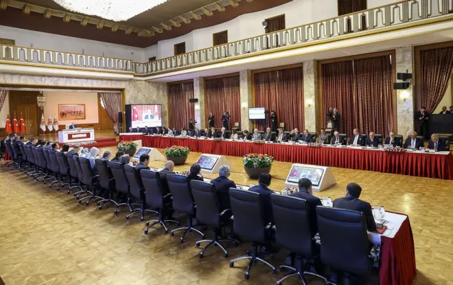 TBMM Komisyon'un toplantı görüntüsü dikdörtgen şeklinde yanyana uzun masalarda oturan takım elbiseli vekiller görünüyor. 