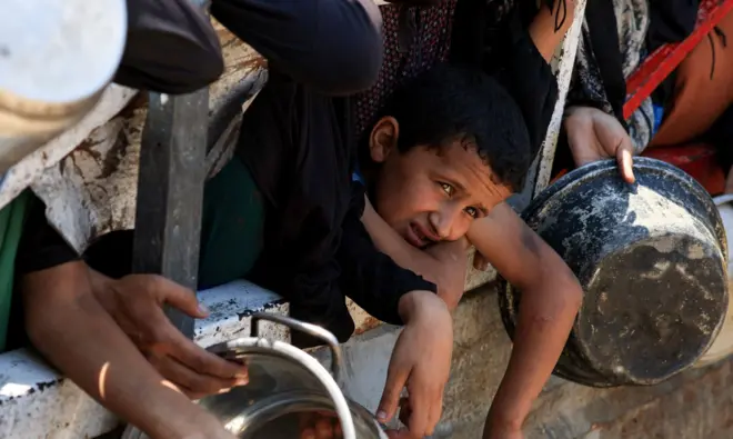 Chłopiec przygląda się, jak Palestyńczycy gromadzą się, by otrzymać jedzenie z kuchni charytatywnej, w obliczu głodu, Gaza, 25 lipca 2025 r.