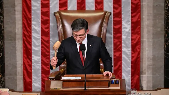 마이크 존슨이 검은색 정장과 빨간색 넥타이를 입고 미국 국기 앞에서 초대형 법안을 통과시키는 순간