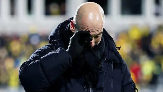 Pep Guardiola wear black winter jacketas e use im hand bl;ock im eyes in sadness.