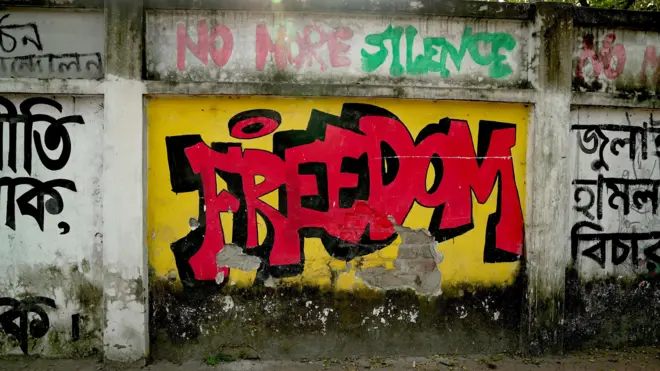 Mural painted on a wall reads "FREEDOM" in bright red letters, on a yellow background. Above that text are the words "No more silence".