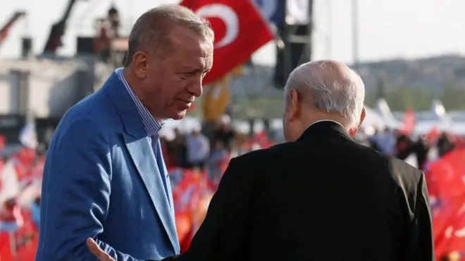 Miting alanında sahnede mavi cekeli Erdoğan yandan görünüyor yüzü arkası dönük siyah cekeli Bahçeli'ye dönük. 7 Mayıs 2023. 