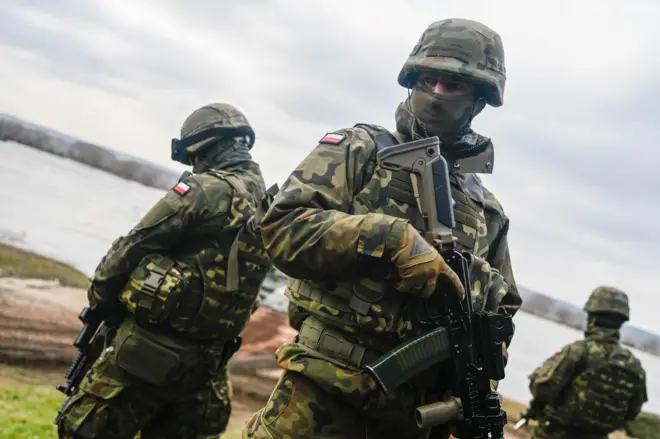 Polscy żołnierze stoją na warcie, gdy inni żołnierze przeprawiają czołgi przez Wisłę podczas ćwiczeń obronnych NATO DRAGON-24