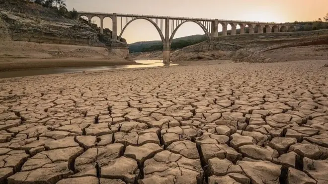 Parched and cracked ground is seen at twilight in front of a viaduct in Entrepenas reservoir, Spain.