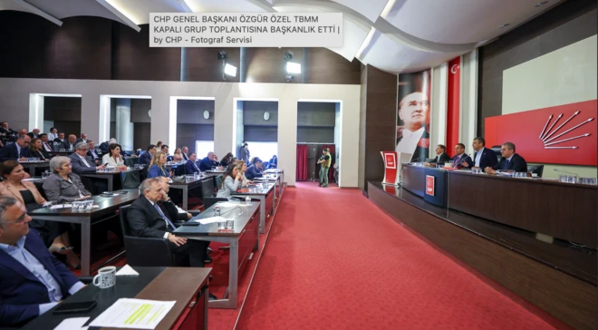 Kırmızı bir halı kürsü ve oturan siyasetçileri ayırıyor. Özgür Özel kürsüde masada oturuyor.