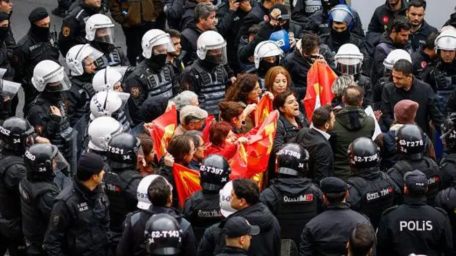 Kırmızı bayrak tutan yaklaşık 10 kişilik bir grup onlarca siyah giyimli çevik kuvvet polisiyle çevrelenmiş. 