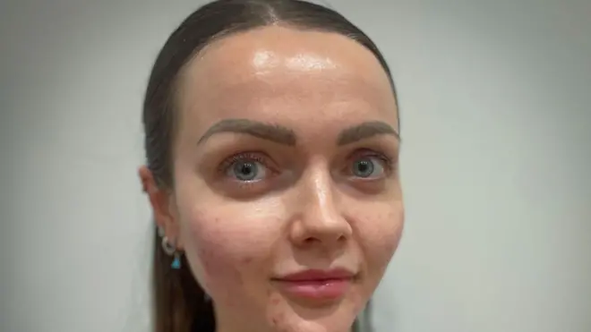 ਐਬੀ ਦੇ ਵਾਲ ਲੰਬੇ ਭੂਰੇ ਹਨ ਅਤੇ ਉਹ ਸਿੱਧਾ ਕੈਮਰੇ ਵੱਲ ਦੇਖ ਰਹੀ ਹੈ।