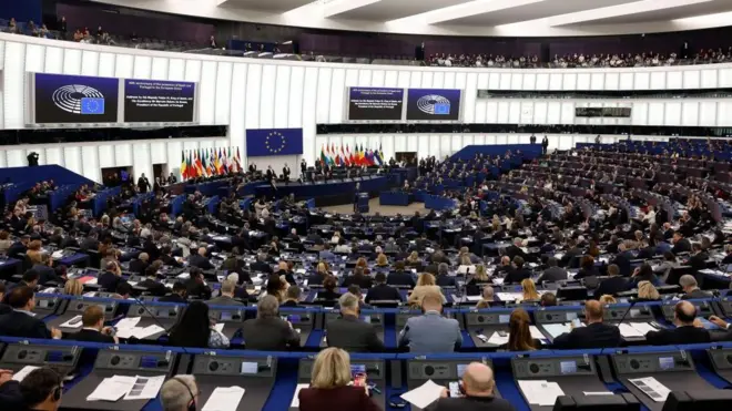 広い議事堂に青い議席がすり鉢状に並び、欧州議会議員たちが書類を前にして前方の議長席を見下ろしている