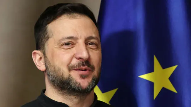 يقف الرئيس الأوكراني فولوديمير زيلينسكي مرتدياً قميصاً أسود، بجوار علم الاتحاد الأوروبي أثناء وصوله للقاء المستشار الألماني أولاف شولتز في مؤتمر ميونيخ للأمن الحادي والستين في 15 فبراير/شباط 2025 في ميونيخ، ألمانيا.