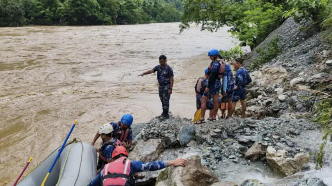 Group of people in helmets and life vests preparing a raft by a fast-flowing river in Nepal.