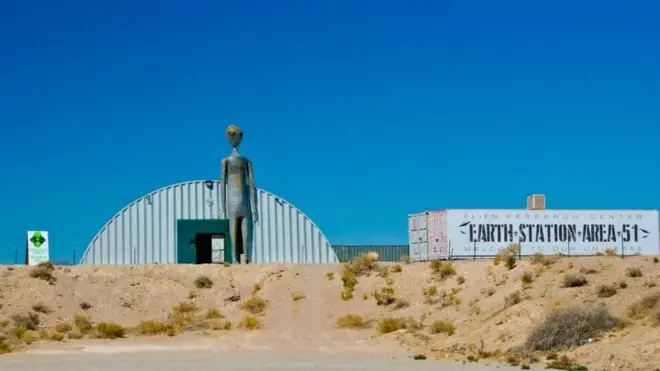 Araştırma merkezinin önünde dev bir gir uzaylı heykeli var. Yanındaki bir konteyner üzerinde büyük harflerle "Dünya-istasyon-51. Bölge" yazıyor.
