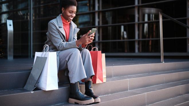 Mulher negra sentada com sacolasganhar na betanocompras