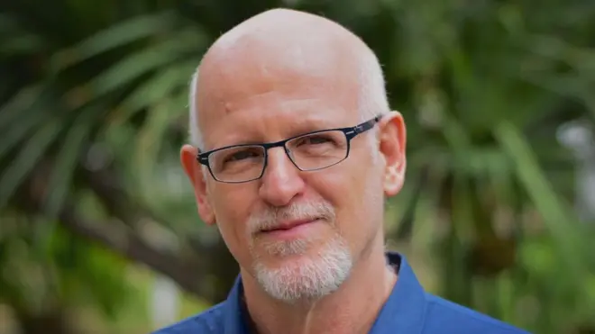 Daniel Becker é um homemjogar demo blazepele clara, careca, com cavanhaque e bigode brancos. Está usando um óculos retangularjogar demo blazearo escuro e uma camisa azul. 