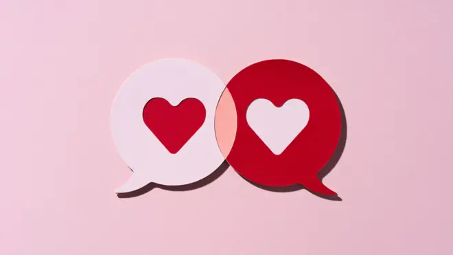 Recorte em papel de dois balões de conversa em forma de coração vermelho, atraídos um pelo outro, sobre fundo rosa