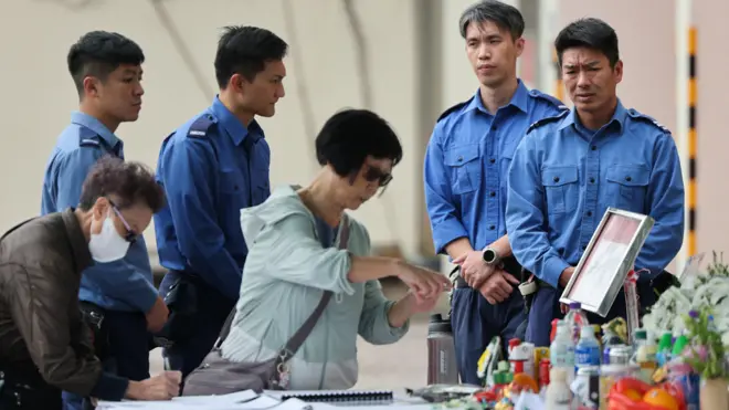 在沙田消防局入口处，消防员们正在哀悼，人们继续献花悼念在太埔宏福苑火灾中殉职的消防员何伟豪（2/12/2025）