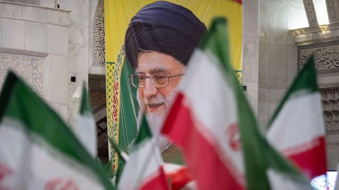 Старый человек в иранском религиозном головном уборе среди иранских флагов