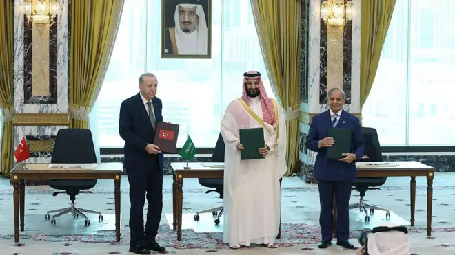 Cumhurbaşkanı Erdoğan, Muhammed bin Selman ve Şahbaz Şerif ayakta ellerindeki anlaşma ile poz veriyor