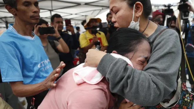 Mulher é consolada por duas pessoas enquanto chora e busca informações sobre um conhecido que está desaparecido após os terremotos