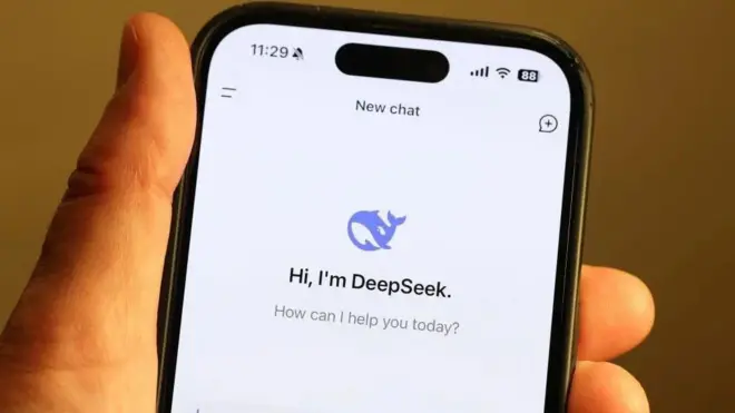 Рука, держащая телефон, на котором открыт чат с DeepSeek. Там виден логотип в виде синего кита и надпись Hi, I'm DeepSeek. How can I help you today? («Привет, я DeepSeek. Чем я сегодня могу помочь?»)