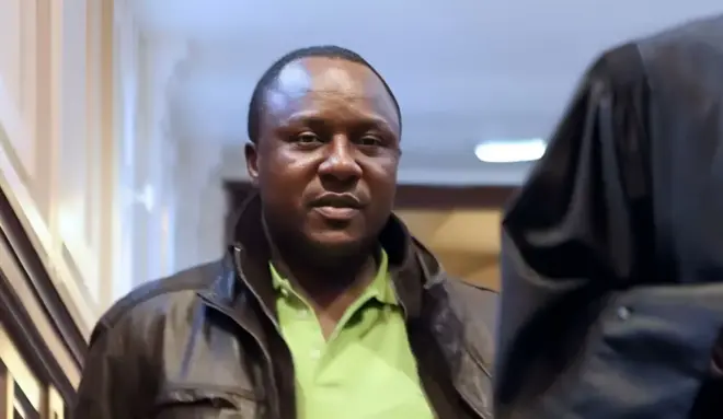 Claude Muhayimana yambaye ijaketi y'umukara n'ishati y'icyatsi kibisi