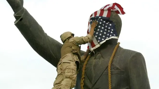 جندي أمريكي يضع علم أمريكا على وجه تمثال صدام حسين