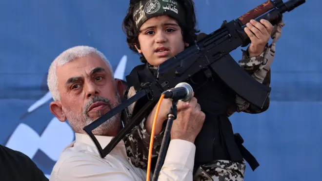 Hamas leader Yahya Sinwar holds the child of an Al-Qassam Brigades fighter, who was killed in the recent fighting with Israel, with a Kalashnikov rifle in his hand during a rally in Gaza City on May 24, 2021