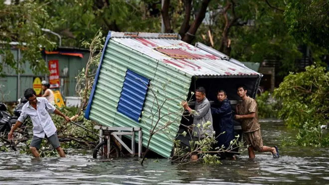 စူပါတိုင်ဖွန်းမုန်တိုင်း ယာဂီ တိုက်ခတ်အပြီး အပျက်အစီးတွေကို ဒူးခေါင်းနီးနီး ရောက်နေတဲ့ ရေတောထဲမှာ သယ်ယူနေကြတဲ့ အမျိုးသား ၄ ဦးကို တွေ့ရတာဖြစ်ပါတယ်။ သူတို့အနောက်မှာတော့ မုန်တိုင်းကြောင့် ပြိုလဲသွားတဲ့သစ်ပင်အချို့ကို မြင်တွေ့ရပါတယ်။ 