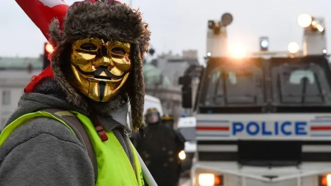 A masked protestor stands in front of a police vehicle in Paris on 5 January 2019, during a rally by yellow vest "Gilets Jaunes" anti-government protesters