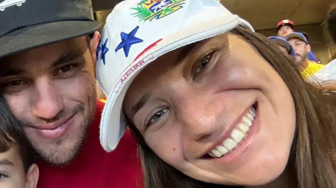 Claudia Rodríguez, derecha, con una gorra blanca, sonríe a cámara en un estadio junto a un hombre y un niño.