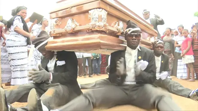 un groupe de danseurs portent le cercueil d'un défunt en rythme au Ghana.