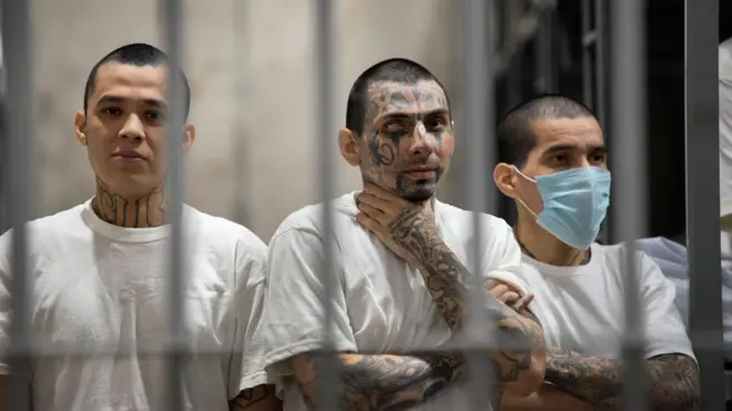 Three inmates covered with tattoos, behind bars at Cecot prison, El Salvador