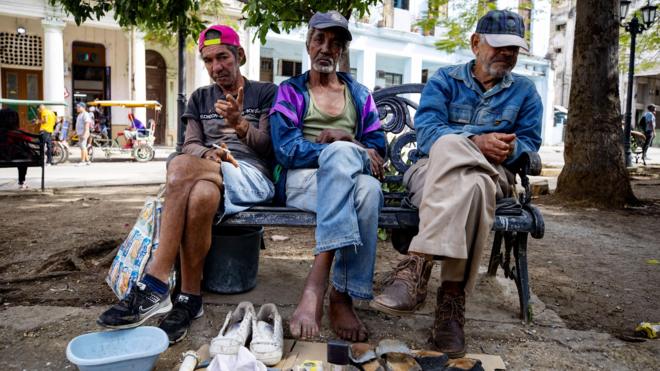 Três cubanos vendendo sapatos e sandálias numa rua de Havana